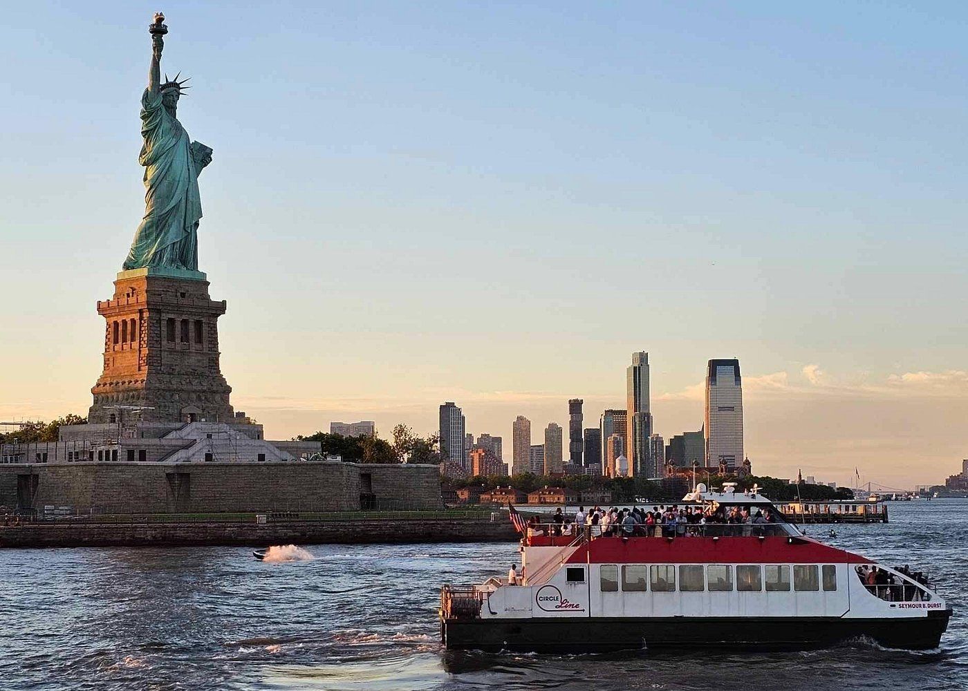 Cruise boat in front of the Statue of Liberty at sunset